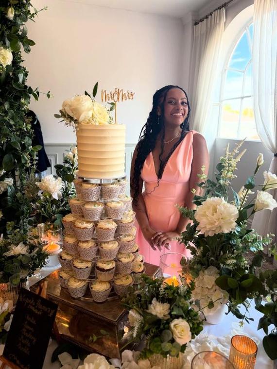 Lori-Anne Brandt standing beside a buttercream wedding cake on a tower of cupcakes